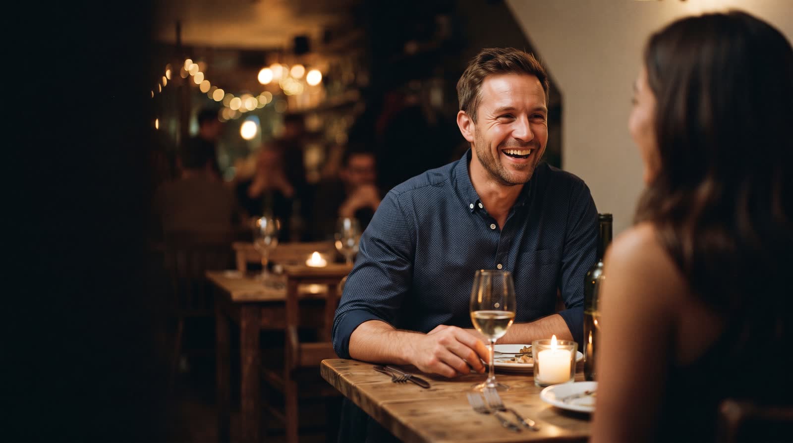 A man laughing across a candlelit table on a date that is going well.