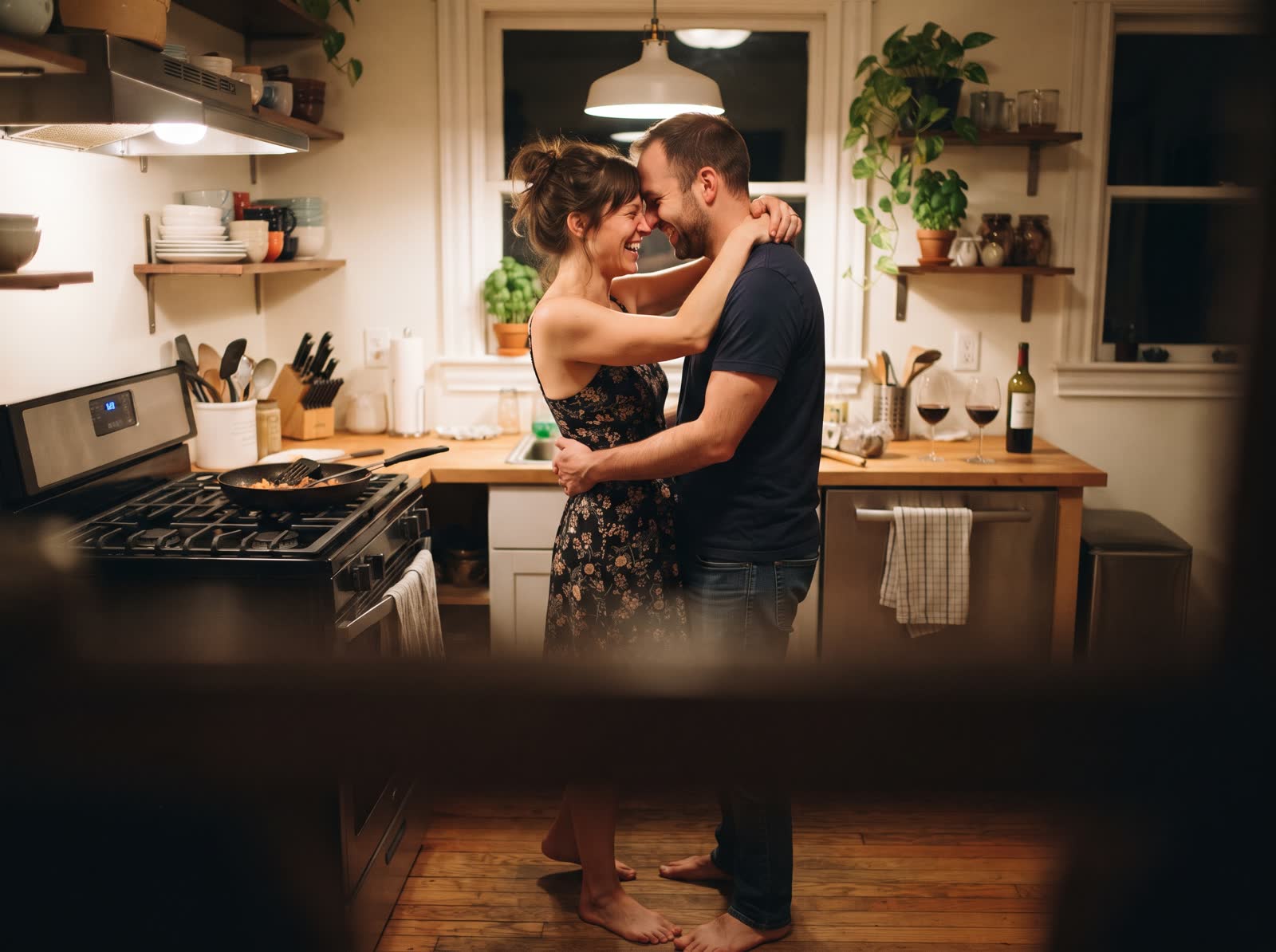 A couple slow dancing in their kitchen, foreheads together, laughing.